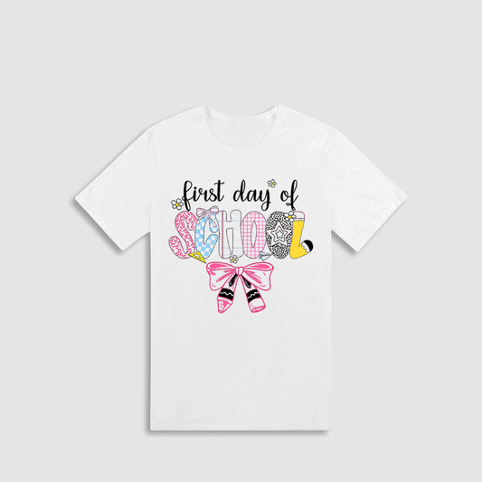 A white t-shirt with a colorful graphic design that says "first day of school" and includes various school-related icons and text.