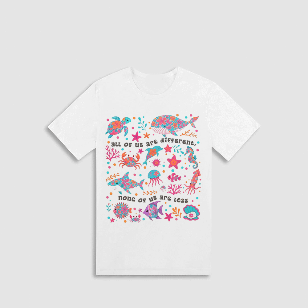 A white t-shirt with a colorful graphic design depicting various marine life, including fish, sharks, and sea creatures, along with the text "all of us are different. none of us are less".