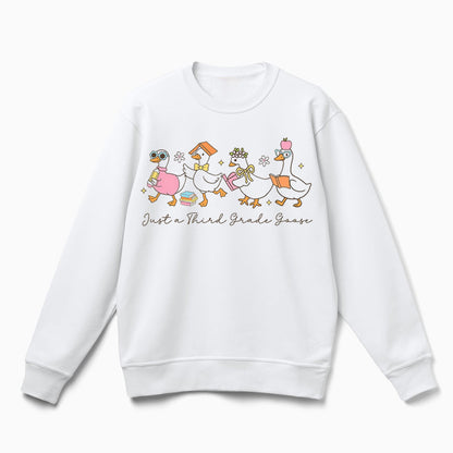 A white sweatshirt with a graphic design featuring a group of cartoon ducks, along with the text "Just a Third Grade Goose" printed on it.