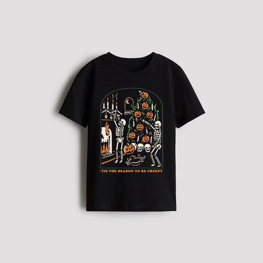 A black t-shirt with a Halloween-themed graphic design featuring a skeleton, jack-o-lanterns, and a fireplace.