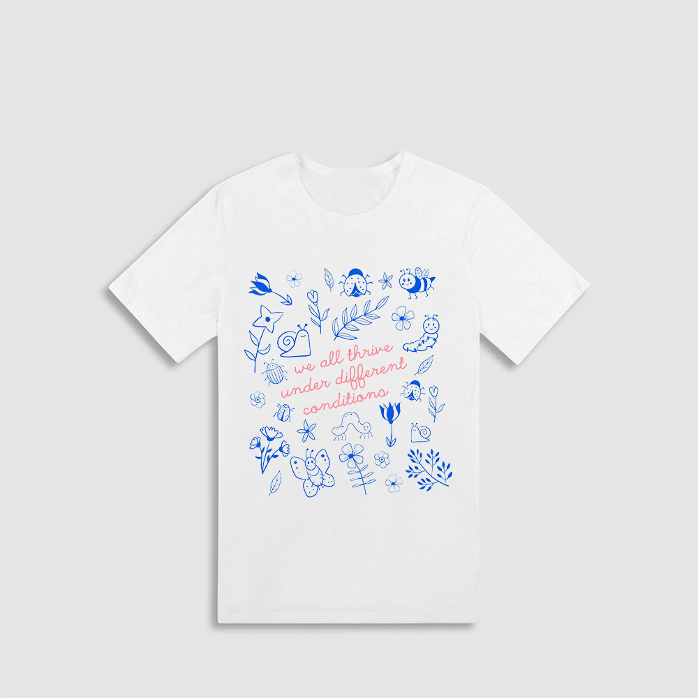 A white t-shirt with a printed design featuring various blue and white illustrations, along with the text "we all thrive under different conditions" printed on it.