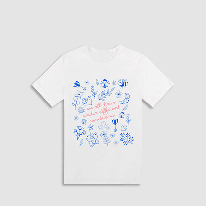 A white t-shirt with a printed design featuring various blue and white illustrations, along with the text "we all thrive under different conditions" printed on it.