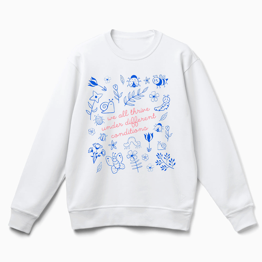 A white sweatshirt with a printed design featuring various blue and white illustrations, along with the text "we all thrive under different conditions" printed on it.
