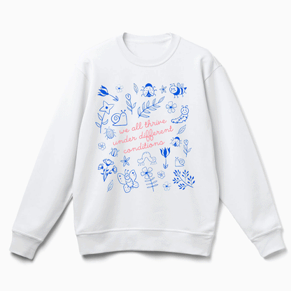 A white sweatshirt with a printed design featuring various blue and white illustrations, along with the text "we all thrive under different conditions" printed on it.