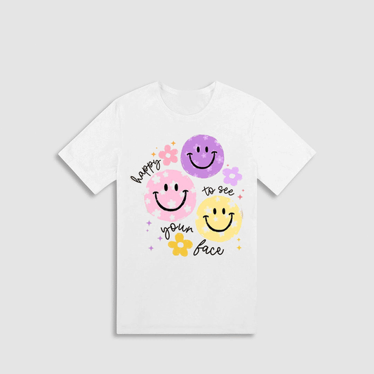 A white t-shirt with a graphic design featuring three smiling faces in different colors - pink, purple, and yellow - along with the text "hope to see your face" written around the edges.