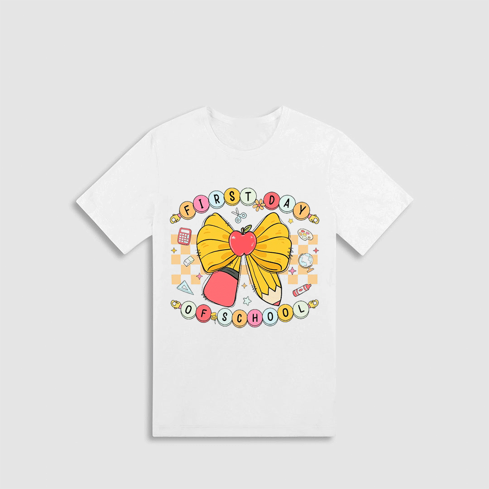 A white t-shirt with a colorful graphic design featuring a yellow bow, a red apple, and various school-related icons.