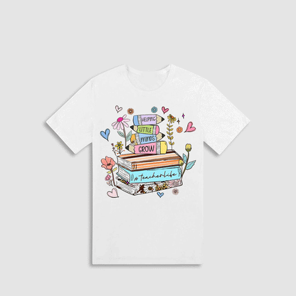 A white t-shirt with a colorful graphic design featuring a stack of books, flowers, and other whimsical elements.