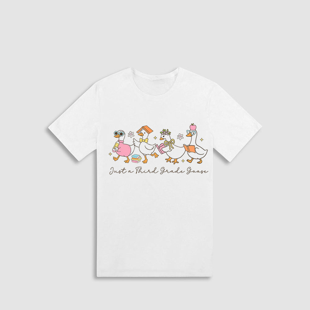 A white t-shirt with a graphic design featuring a group of cartoon ducks and the text "Just a Third Grade Goose" printed on it.