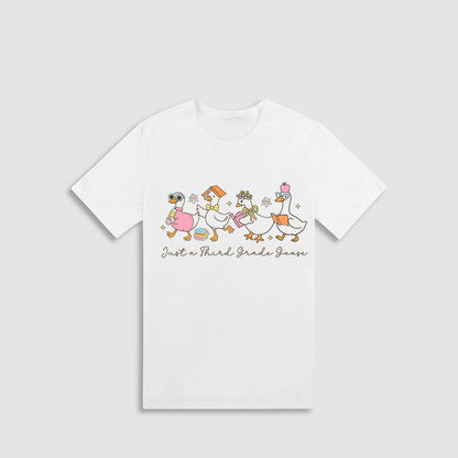 A white t-shirt with a graphic design featuring a group of cartoon ducks and the text "Just a Third Grade Goose" printed on it.
