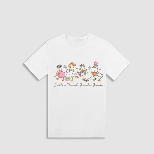A white t-shirt with a graphic design featuring a group of cartoon ducks and the text "Just a Third Grade Goose" printed on it.
