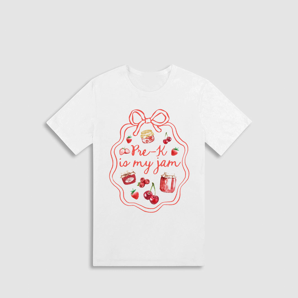 A white t-shirt with a red graphic design featuring a bow, cherries, and a jar of jam, along with the text "Pre-K is my jam" written in a cursive font.
