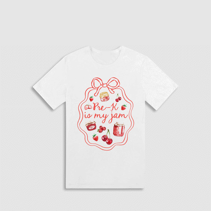 A white t-shirt with a red graphic design featuring a bow, cherries, and a jar of jam, along with the text "Pre-K is my jam" written in a cursive font.