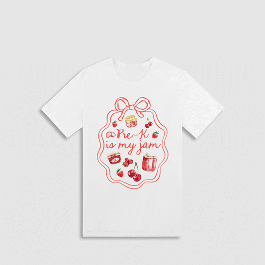 A white t-shirt with a red graphic design featuring a bow, cherries, and a jar of jam, along with the text "Pre-K is my jam" written in a cursive font.