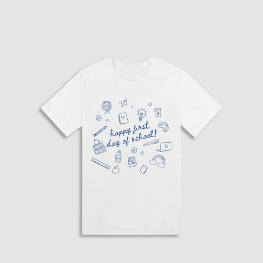 A white t-shirt with a graphic design featuring various school-related items such as a globe, pencil, book, and other school supplies, along with the text "happy first day of school!"