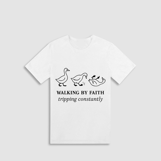 A white t-shirt with a graphic design featuring three cartoon ducks and the text "WALKING BY FAITH TRIPPING CONSTANTLY".