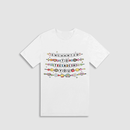 A white t-shirt with a colorful graphic design featuring the text "Enchanted to teach you" surrounded by various decorative elements.