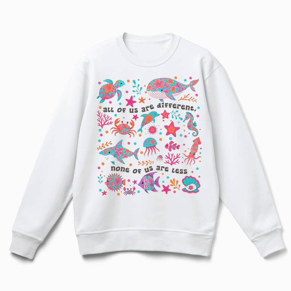 A white sweatshirt with a colorful graphic design featuring various marine life, such as fish, sea creatures, and coral, along with the text "All of us are different none of us are less".