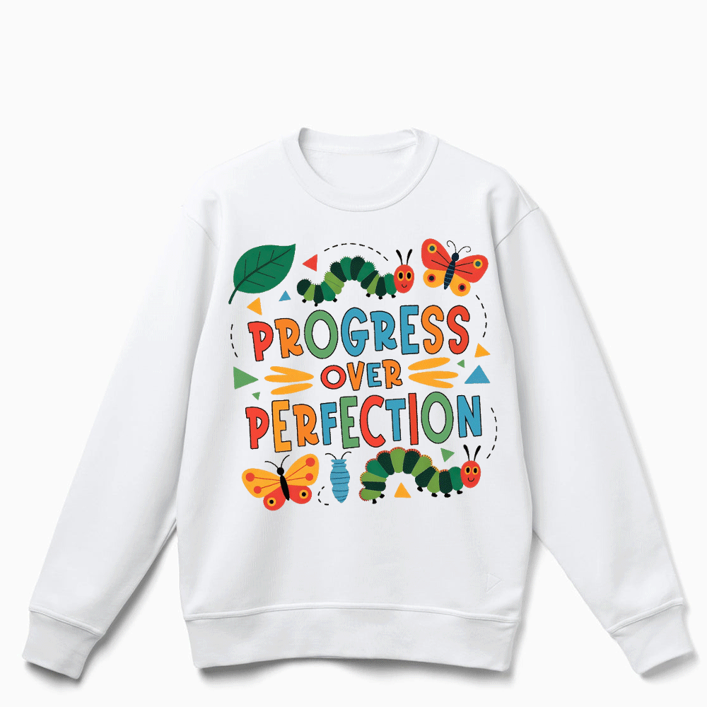 A white sweatshirt with a colorful graphic design featuring butterflies, caterpillars, and the text "PROGRESS OVER PERFECTION".